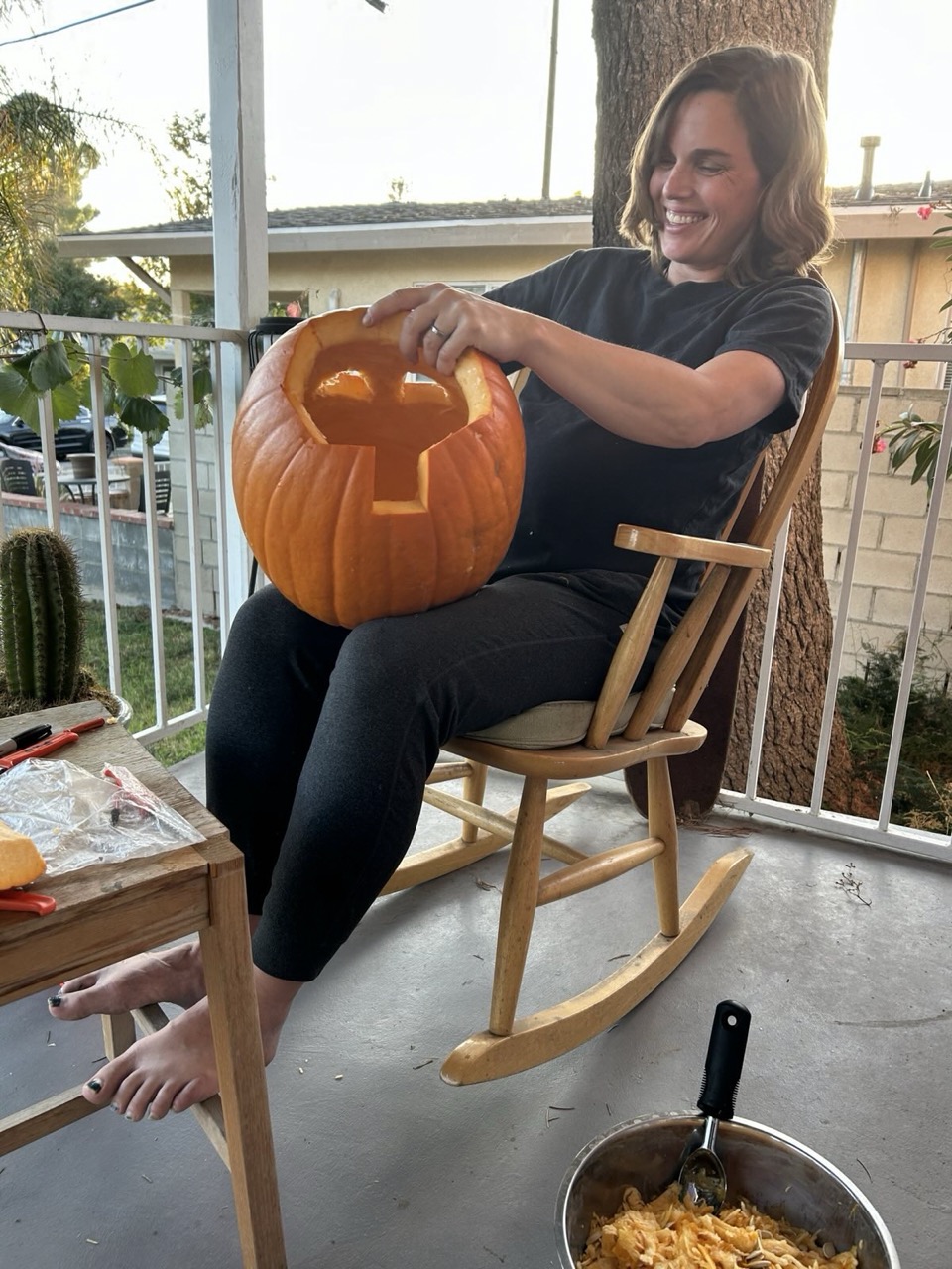 image katie carving a pumpking joyfully while sitting in a rocking chair on the porch.